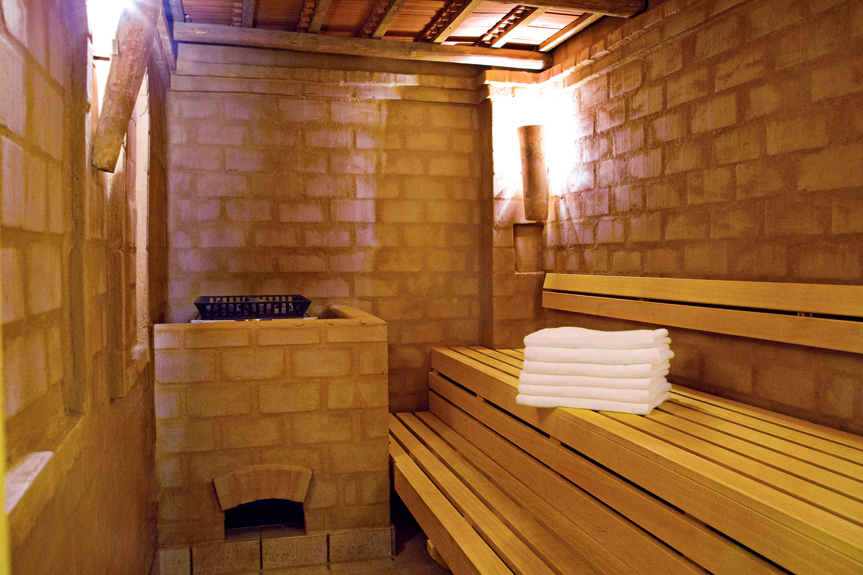 Rustikale Sauna im Hotel Churfürstenhof mit Ziegelwänden, Holzbänken und gestapelten Handtüchern