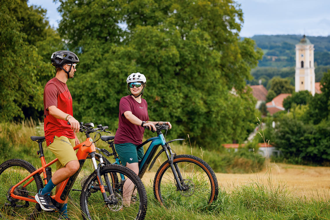 Zwei Radfahrer mit E-Mountainbikes in der Rottaler Landschaft mit Blick auf Kößlarn