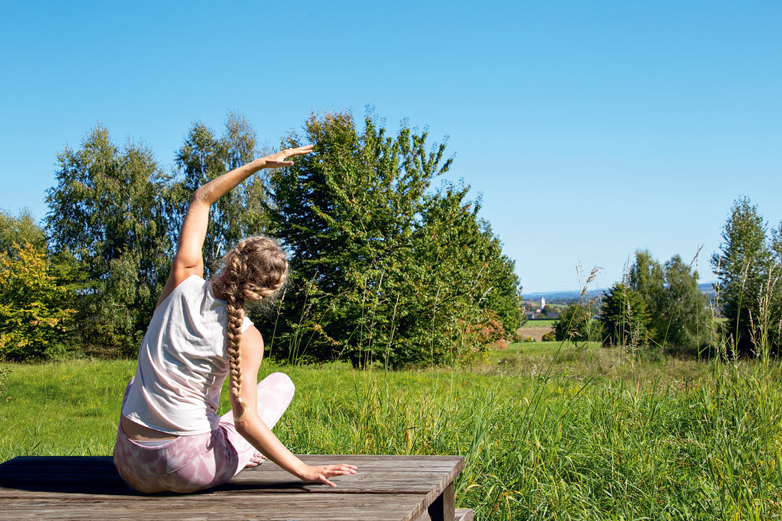 Frau bei Yoga im Grünen auf einer Holzplattform am Rottaler Baum-Yoga-Weg bei Bad Birnbach
