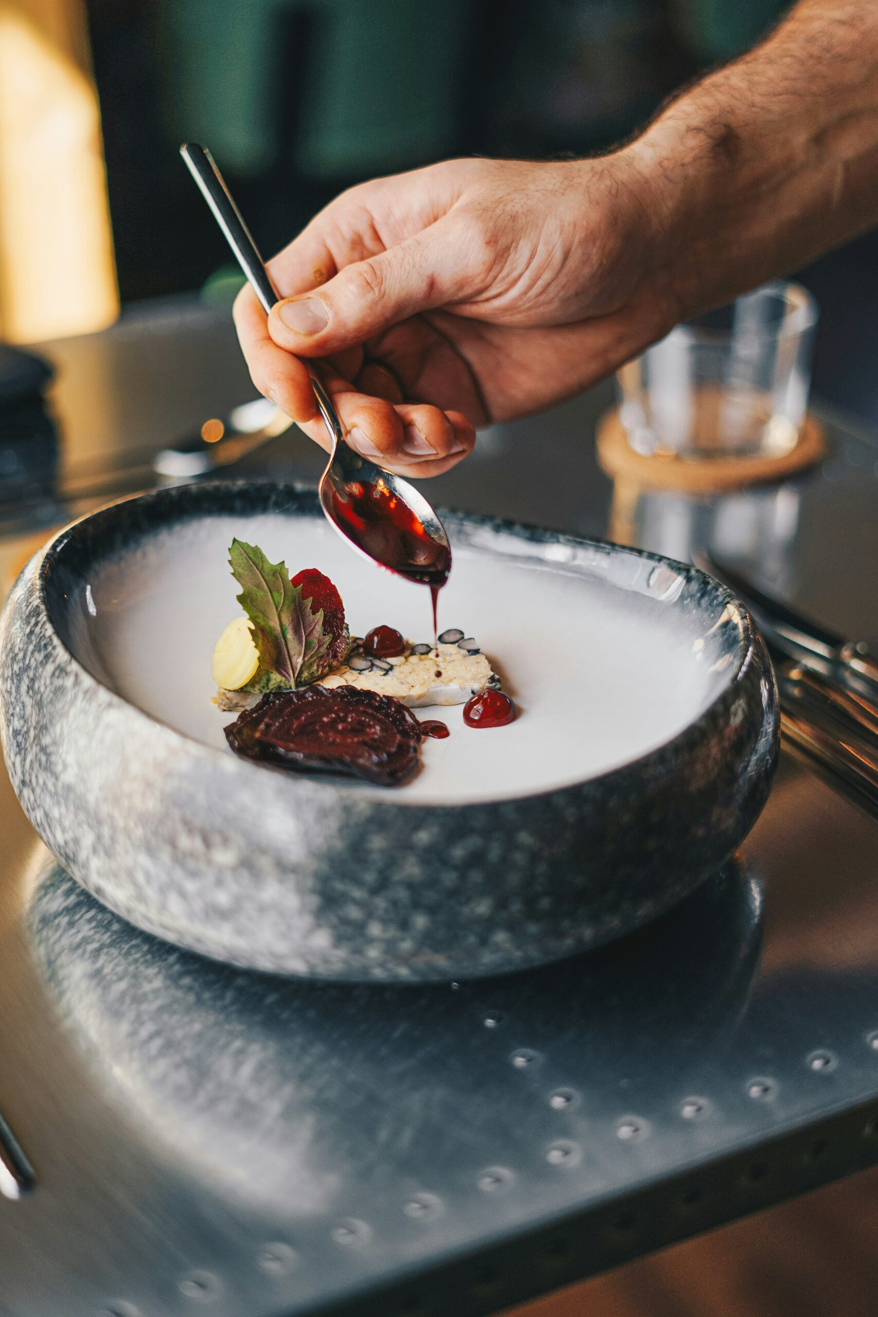 Hand verfeinert ein angerichtetes Gourmetgericht in einer Steinschale mit roter Sauce