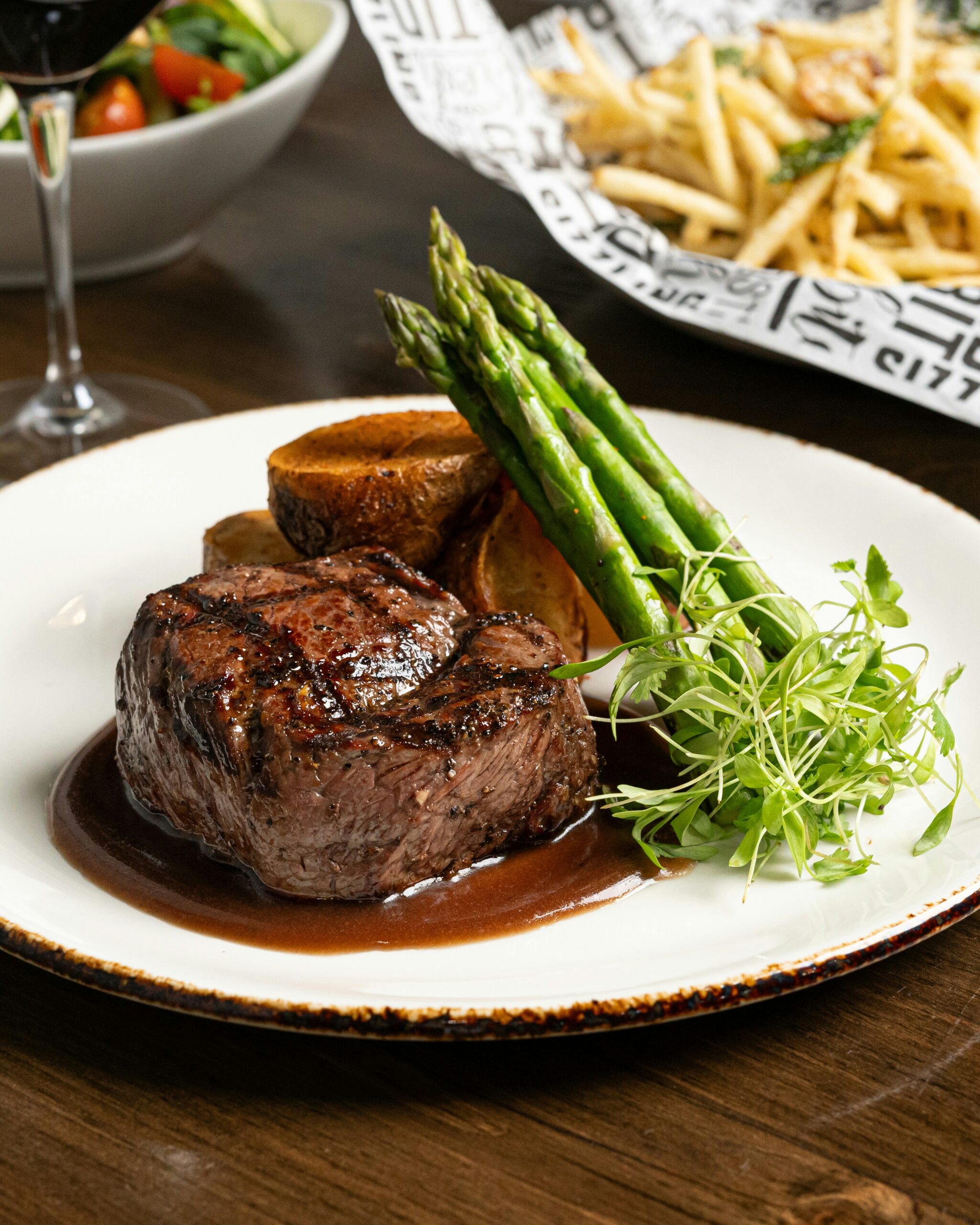 Gegrilltes Rinderfilet mit grünem Spargel, Kartoffeln und Bratensauce, dazu Pommes frites und Salat