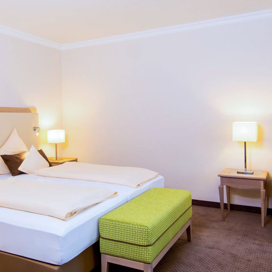 Doppelbett mit weißer Bettwäsche und grüner Sitzbank im Zimmer Baroness, Hotel Churfürstenhof Bad Birnbach