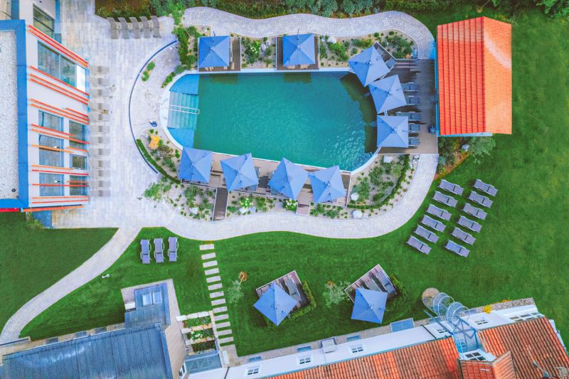 Luftaufnahme des Außenpools mit blauen Sonnenschirmen, Liegen und Garten am Hotel Churfürstenhof
