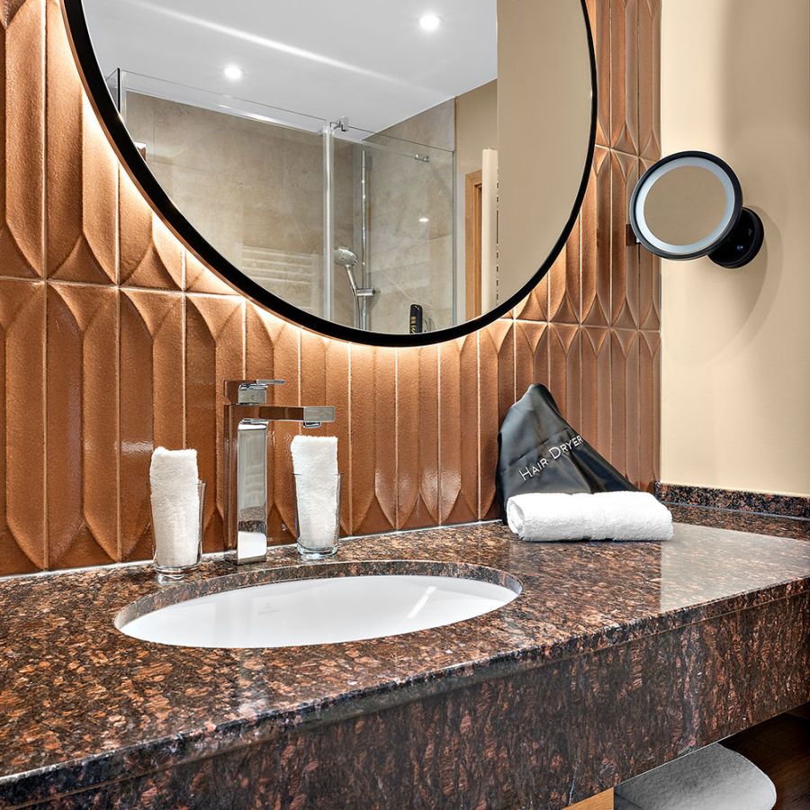 Badezimmer im Zimmer Prinzess mit Granit-Waschtisch, rundem Spiegel und Kupferfliesen, Hotel Churfürstenhof Bad Birnbach