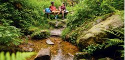 Radler-Paar rastet auf einer Bank am Bach im Wald bei Bad Birnbach, E-Bike im Hintergrund