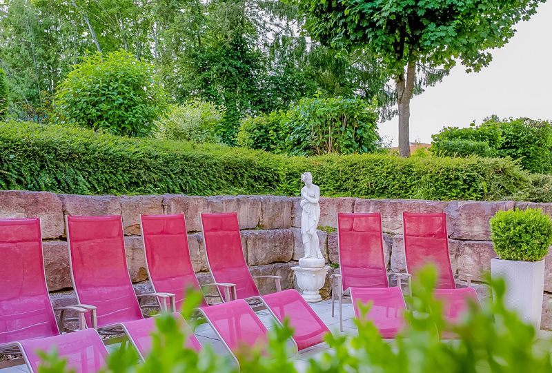 Pinke Gartenliegen vor Natursteinmauer und weißer Statue im Garten des Hotel Churfürstenhof