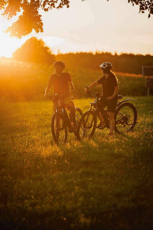 Zwei Radfahrer mit Mountainbikes auf einer Wiese im goldenen Licht des Sonnenuntergangs