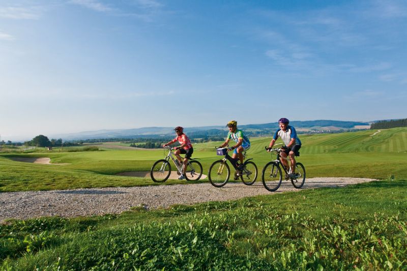 Drei Radfahrer auf einem Kiesweg durch den Golfpark bei Bad Birnbach unter blauem Himmel