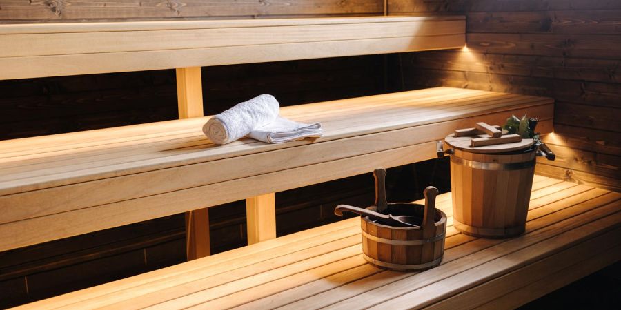Finnische Sauna aus hellem Holz mit gerolltem Handtuch und Aufgusskübeln auf der Bank