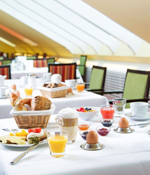 Gedeckte Frühstückstische mit Brötchenkorb, Eiern und Saft im hellen Frühstücksraum des Hotel Churfürstenhof
