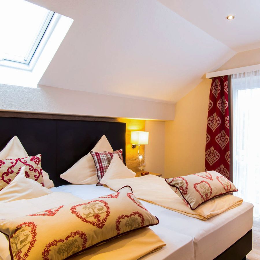 Gemütliches Doppelbett mit Herzkissen unter Dachschräge im Bad Birnbacher Chalet des Hotel Churfürstenhof