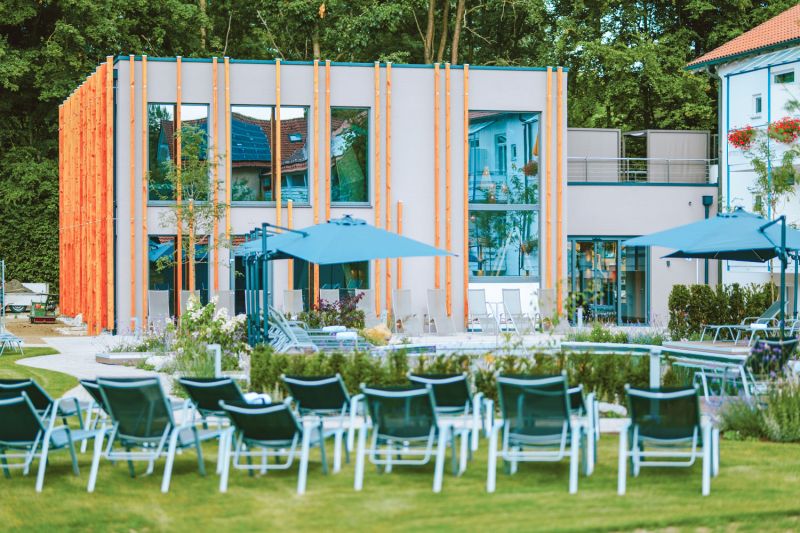 Naturpool des Hotel Churfürstenhof mit Sonnenschirmen und Liegen vor der Hotelfassade, umrahmt von Blumen