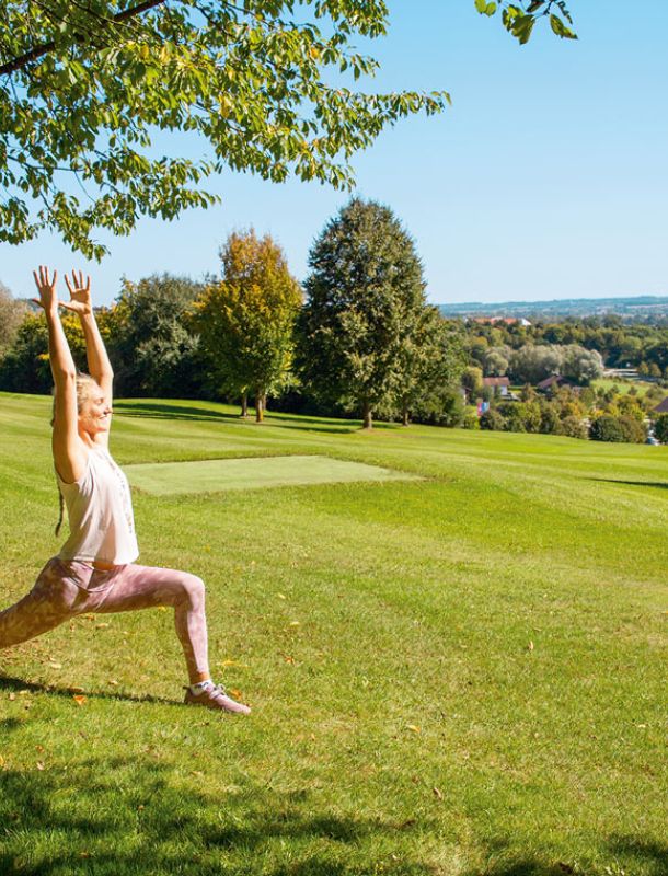 Frau bei einer Yoga-Übung unter einem Baum am Rottaler Baum-Yoga-Weg mit Blick über Bad Birnbach