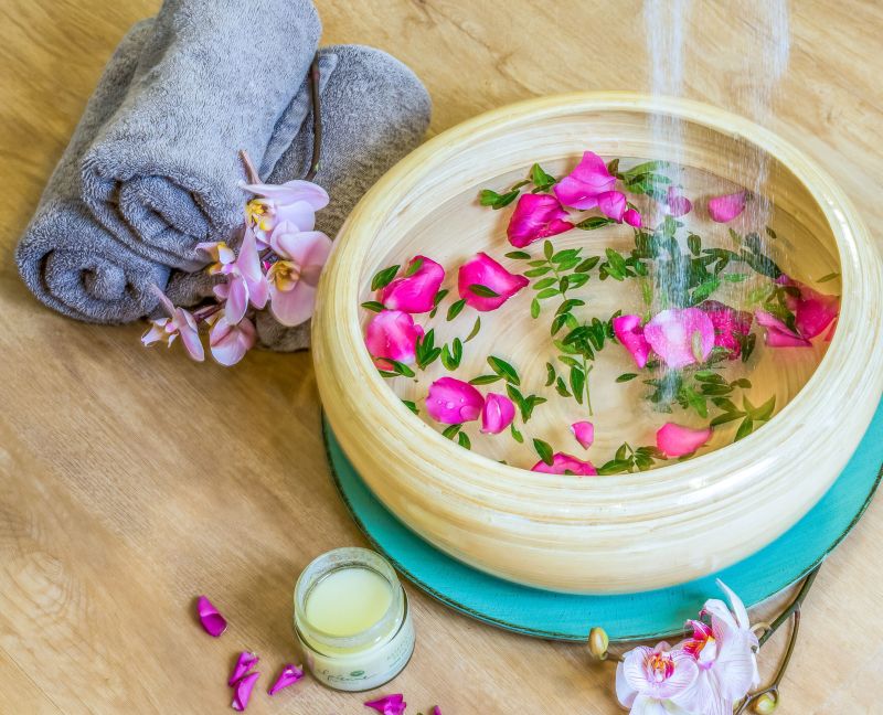 Wellness-Arrangement mit Rosenblüten in einer Holzschale, Handtüchern und Orchideen
