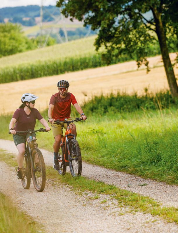 Paar auf E-Bikes radelt über einen Feldweg durch die hügelige Landschaft des Rottals