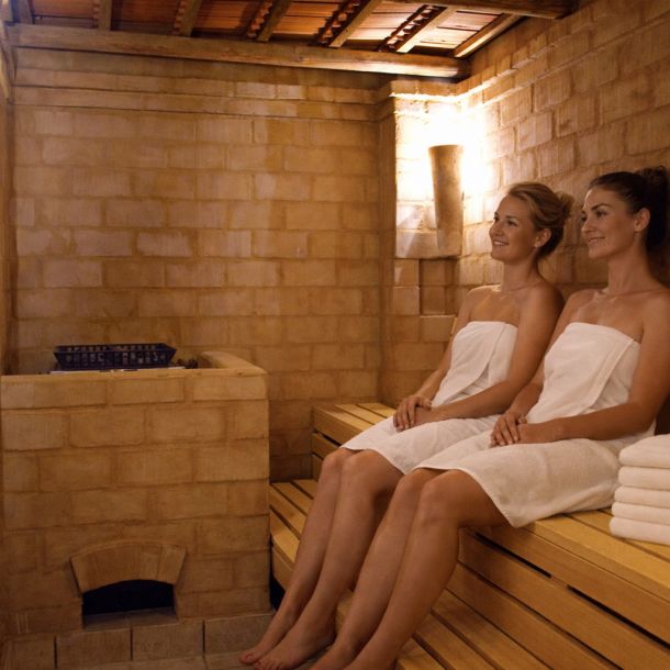 Zwei Frauen in Handtüchern entspannen auf der Holzbank der Lehmsauna im Hotel Churfürstenhof