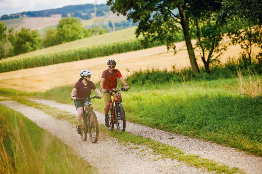 Couple on e-bikes cycling along a country lane through the rolling Rottal landscape